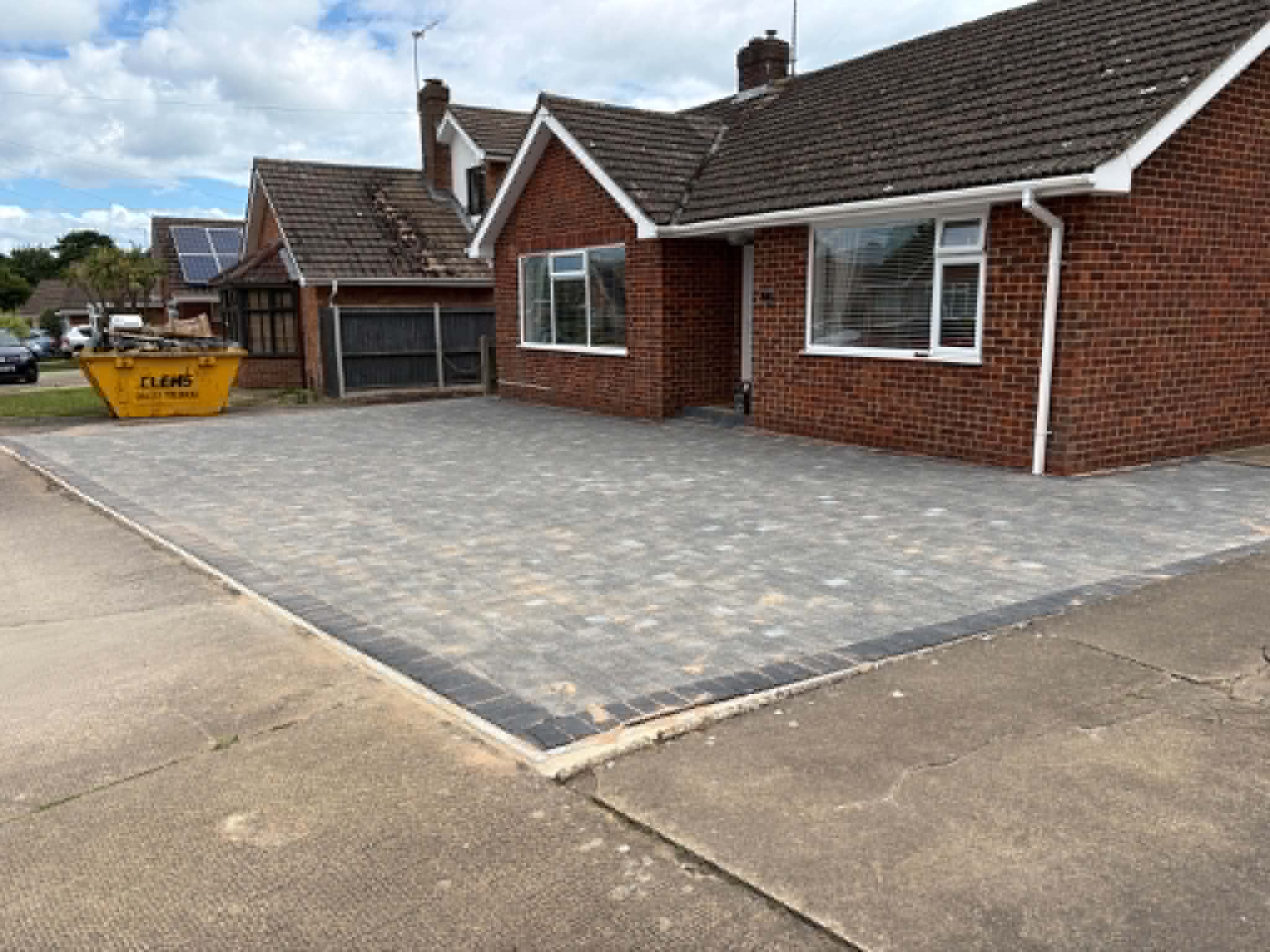 Completed large grey paved driveway outside a red-brick bungalow